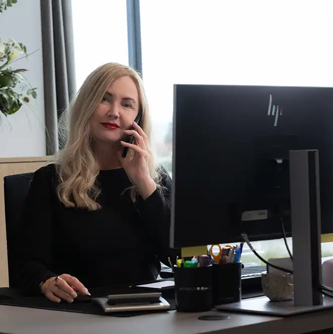 Eine TRUST Personal Mitarbeiterin telefoniert am Schreibtisch vor ihrem Bildschirm im modernen Büro.