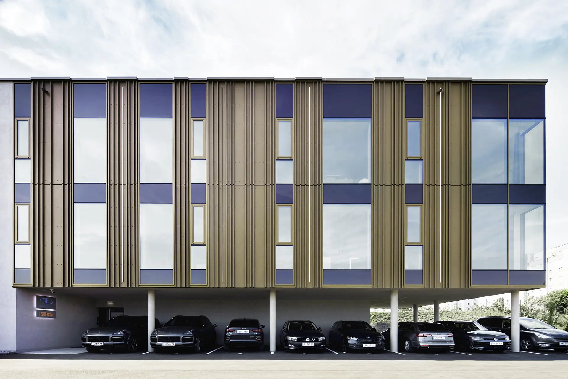 Frontalansicht der modernen Fassade des TRUST Personal Gebäudes mit überdachten Kunden- und Mitarbeiterparkplätzen.