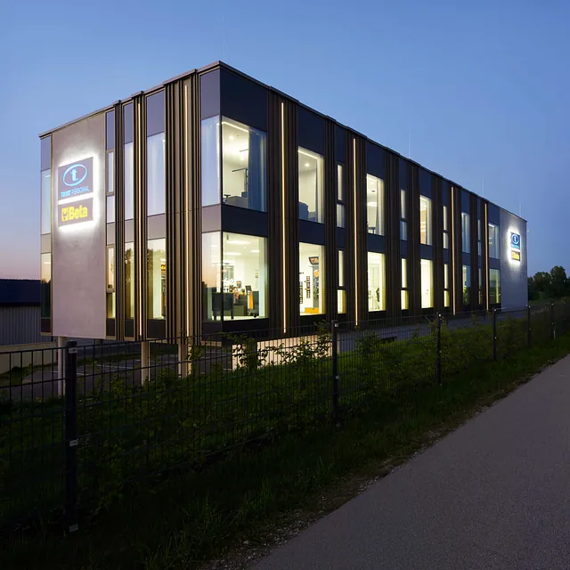 Modernes Firmengebäude von TRUST Personal mit beleuchteter Fassade und großen Fensterfronten bei Abenddämmerung.
