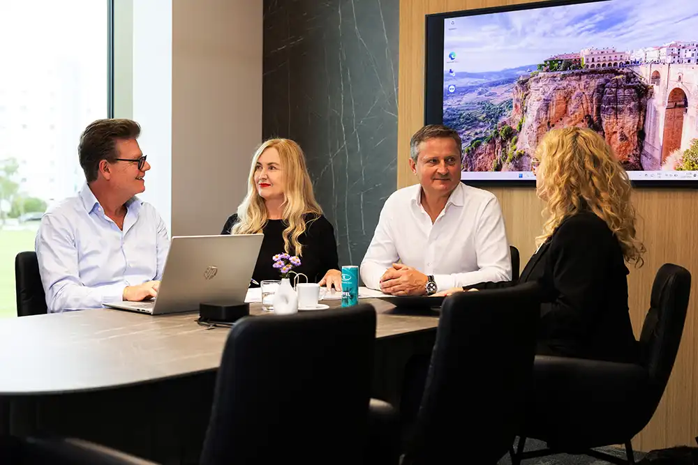 Vier Personen bei einer strategischen Besprechung am Konferenztisch mit Laptop im modernen Meetingraum von TRUST Personal.