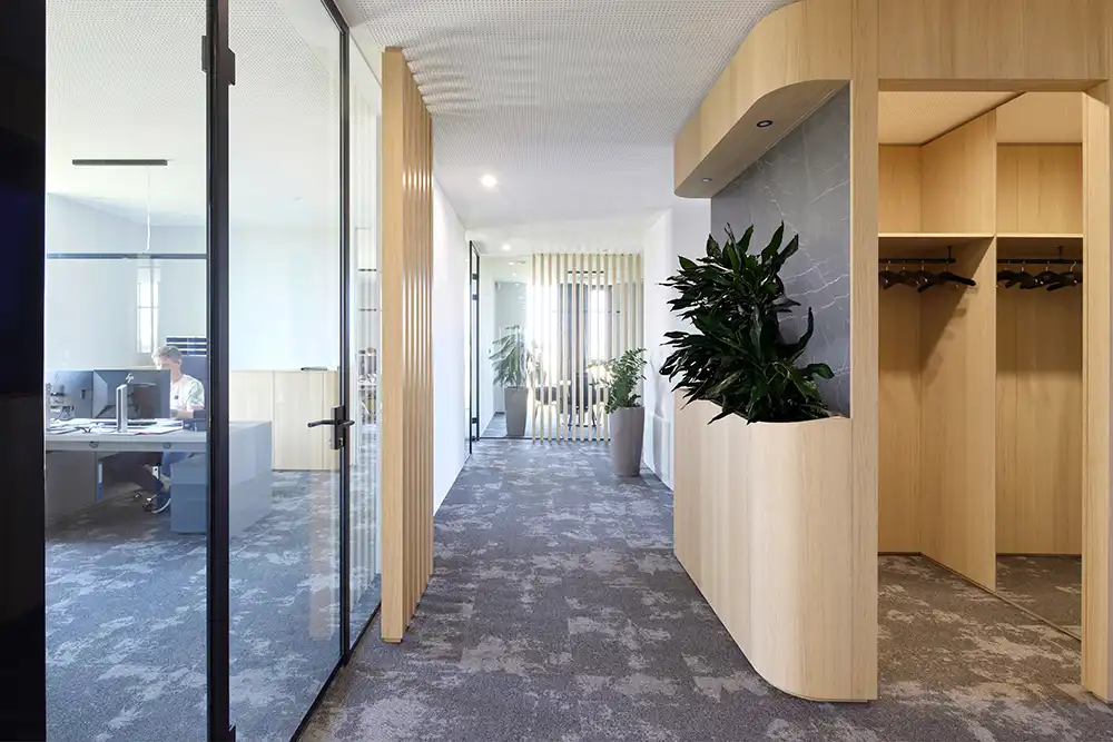 Flur im Büro von TRUST Personal mit integrierter Holz-Garderobe und Blick durch eine Glaswand in ein Einzelbüro.